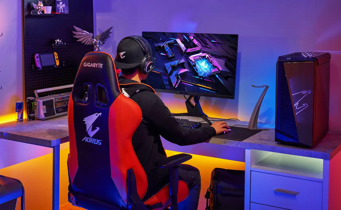 Setup gamer completo mostrando a traseira da cadeira gamer preta com detalhes em vermelho.