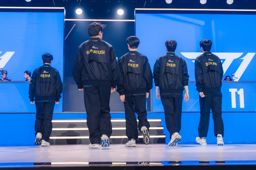 Pro players da T1 em stage de costas na ordem: Keria, Gumayusi, Faker, Oner e Doran