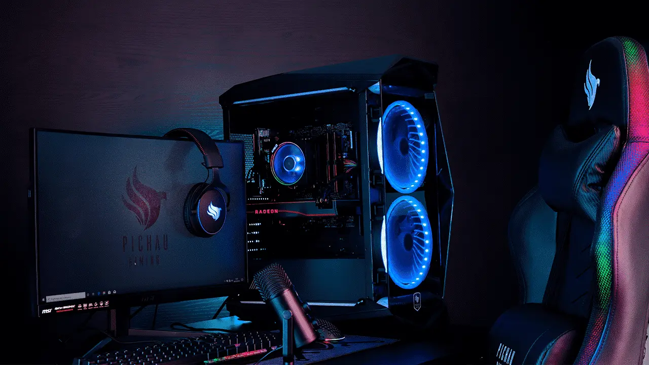Setup gamer com computador de mesa iluminado por luzes LED azuis, monitor, teclado, headset, microfone e cadeira gamer em ambiente escuro.