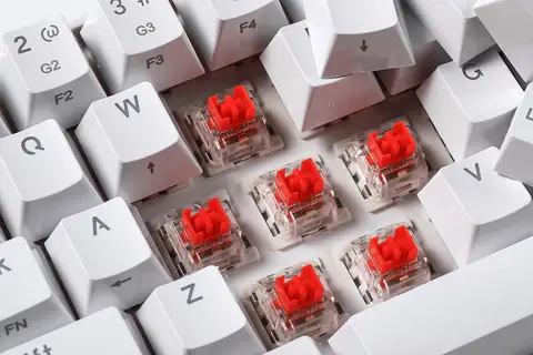 Teclado mecânico com algumas teclas desmontadas, mostrando o switch de cor vermelha.